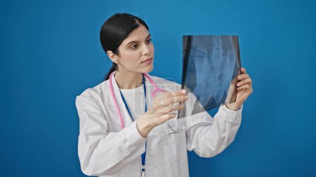 Téléchargez les photos : Jeune belle hispanique femme médecin à la recherche de rayons X sur fond bleu isolé - en image libre de droit
