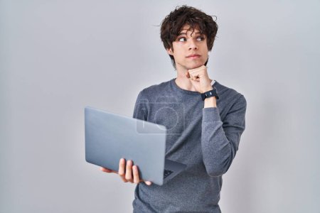 Photo for Young man working using computer laptop serious face thinking about question with hand on chin, thoughtful about confusing idea - Royalty Free Image