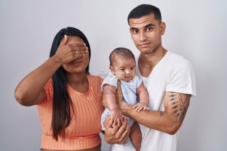 Téléchargez les photos : Jeune couple hispanique avec bébé debout ensemble sur fond isolé couvrant les yeux avec la main, l'air grave et triste. concept de non-visibilité, de dissimulation et de rejet - en image libre de droit