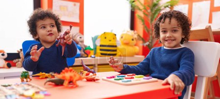 Foto de Adorables niños afroamericanos jugando con el juego de rompecabezas de matemáticas y el juguete de dinosaurio en el jardín de infantes - Imagen libre de derechos