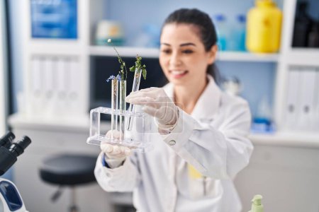 Photo for Young beautiful hispanic woman scientist holding test tubes with flowers at laboratory - Royalty Free Image