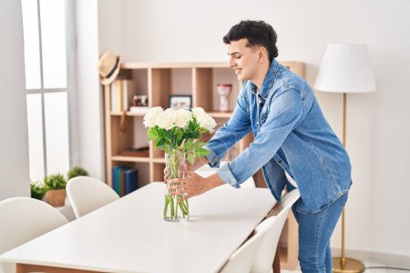 Photo for Young non binary man smiling confident putting flowers on table at home - Royalty Free Image