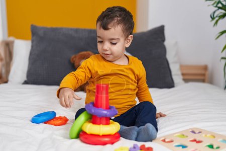 Téléchargez les photos : Adorable garçon hispanique jouant avec cerceaux jeu assis sur le lit dans la chambre - en image libre de droit