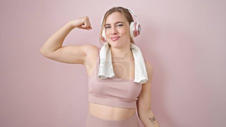 Photo for Young blonde woman listening to music doing strong gesture with arm over isolated pink background - Royalty Free Image