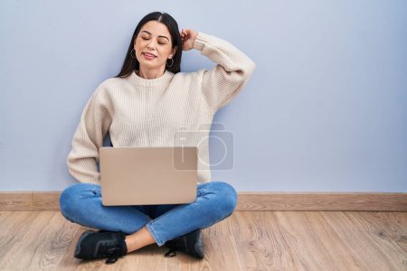 Téléchargez les photos : Jeune femme utilisant un ordinateur portable assis sur le sol à la maison étirant le dos, fatigué et détendu, endormi et bâillant tôt le matin - en image libre de droit