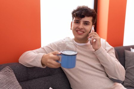 Photo for Non binary man talking on smartphone drinking coffee at home - Royalty Free Image