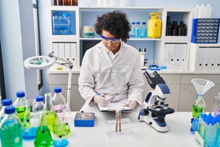 Téléchargez les photos : Young hispanic man wearing scientist uniform measuring sample at laboratory - en image libre de droit