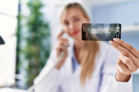 Téléchargez les photos : Young blonde woman wearing dentist uniform talking on the telephone holding xray at clinic - en image libre de droit