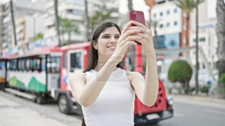 Foto de Joven hermosa mujer hispana sonriendo con confianza grabación de vídeo por teléfono inteligente en la calle - Imagen libre de derechos