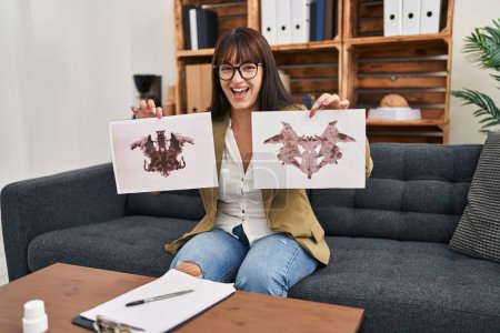 Photo for Young therapist woman working with rorschach test at psychology clinic smiling and laughing hard out loud because funny crazy joke. - Royalty Free Image