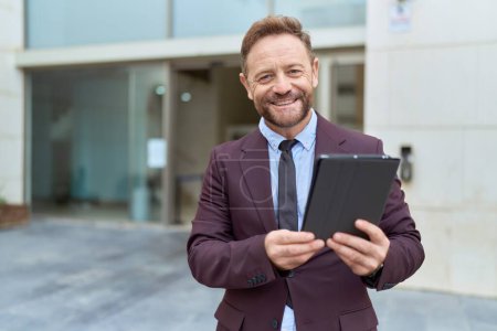 Téléchargez les photos : Homme d'affaires du Moyen Âge avec barbe travaillant à l'extérieur en utilisant une tablette regardant positif et heureux debout et souriant avec un sourire confiant montrant les dents - en image libre de droit