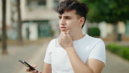Téléchargez les photos : Homme non binaire utilisant un smartphone avec une expression inquiète au parc - en image libre de droit