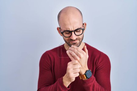 Téléchargez les photos : Jeune homme chauve avec barbe debout sur fond blanc portant des lunettes souffrant de douleur aux mains et aux doigts, inflammation de l'arthrite - en image libre de droit
