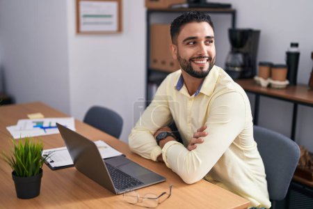Téléchargez les photos : Jeune homme arabe travailleur d'affaires à l'aide d'un ordinateur portable assis sur les bras geste croisé au bureau - en image libre de droit