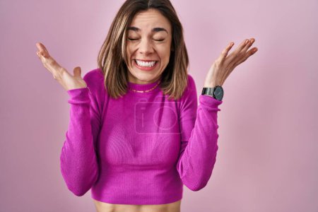 Photo for Hispanic woman standing over pink background celebrating mad and crazy for success with arms raised and closed eyes screaming excited. winner concept - Royalty Free Image