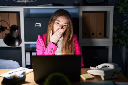 Téléchargez les photos : Jeune femme caucasienne travaillant au bureau la nuit ennuyé bâillement fatigué couvrant la bouche avec la main. agitation et somnolence. - en image libre de droit
