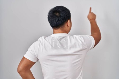 Photo for Young chinese man standing over white background posing backwards pointing ahead with finger hand - Royalty Free Image