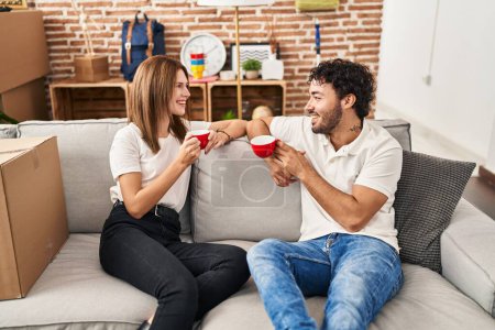 Téléchargez les photos : Homme et femme couple souriant confiance boire du café à la nouvelle maison - en image libre de droit