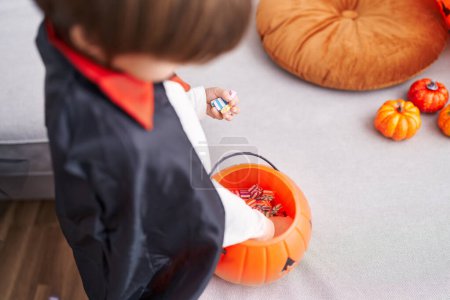 Téléchargez les photos : Adorable garçon caucasien portant costume de vampire tenant des bonbons sur le panier de citrouille à la maison - en image libre de droit