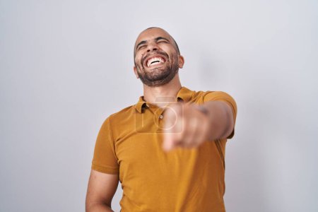 Photo for Hispanic man with beard standing over white background laughing at you, pointing finger to the camera with hand over body, shame expression - Royalty Free Image