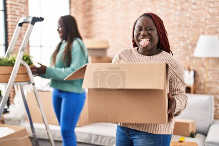 Foto de Dos mujeres africanas se mudan a un nuevo hogar sacando la lengua feliz con expresión divertida. - Imagen libre de derechos