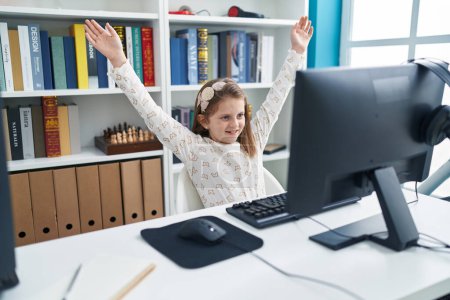 Foto de Adorable estudiante rubia usando computadora con expresión ganadora en el aula - Imagen libre de derechos