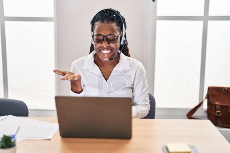 Photo for African woman with braided hair wearing call center agent headset celebrating achievement with happy smile and winner expression with raised hand - Royalty Free Image