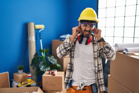 Téléchargez les photos : Jeune homme hispanique avec barbe travaillant à la rénovation de la maison couvrant les oreilles avec des doigts avec une expression agacée pour le bruit de la musique forte. concept sourd. - en image libre de droit