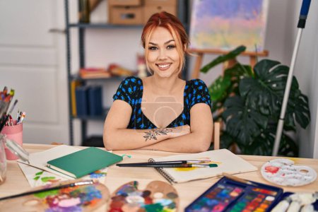Téléchargez les photos : Jeune artiste caucasienne souriante confiante assise avec les bras croisés geste au studio d'art - en image libre de droit