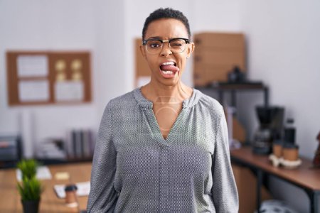 Téléchargez les photos : Femme afro-américaine travaillant au bureau portant des lunettes collant la langue heureux avec une expression drôle. concept d'émotion. - en image libre de droit