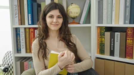 Photo for Young beautiful hispanic woman student smiling confident reading book at library university - Royalty Free Image
