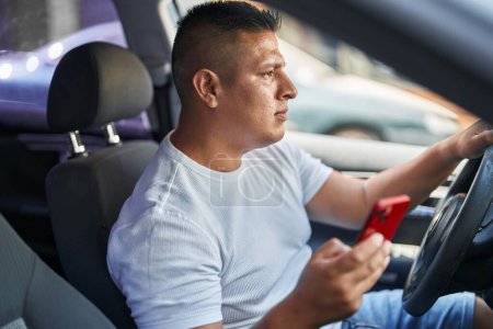 Foto de Hombre latino joven usando teléfono inteligente sentado en el coche en la calle - Imagen libre de derechos