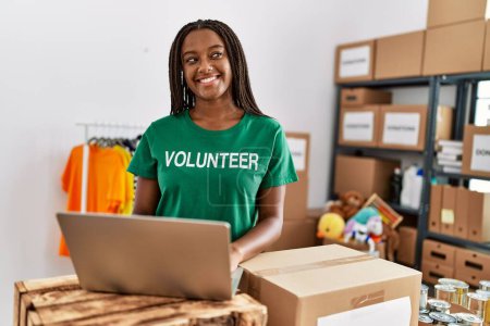 Téléchargez les photos : Jeune femme afro-américaine portant l'uniforme de bénévole travaillant au centre de charité - en image libre de droit