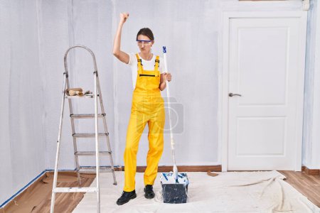 Photo for Young caucasian woman painting walls angry and mad raising fist frustrated and furious while shouting with anger. rage and aggressive concept. - Royalty Free Image