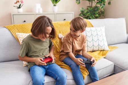 Photo for Adorable boys playing video game sitting on sofa at home - Royalty Free Image