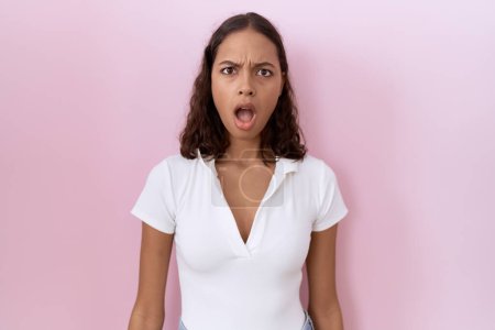 Téléchargez les photos : Jeune femme hispanique portant t-shirt blanc décontracté dans le visage de choc, l'air sceptique et sarcastique, surpris avec la bouche ouverte - en image libre de droit