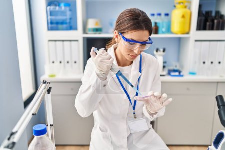 Foto de Mujer hispana joven vistiendo uniforme científico usando pipeta en el laboratorio - Imagen libre de derechos