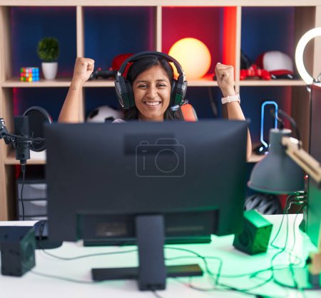 Téléchargez les photos : Jeune belle hispanique femme streamer jouer jeu vidéo avec l'expression gagnante à la salle de jeux - en image libre de droit