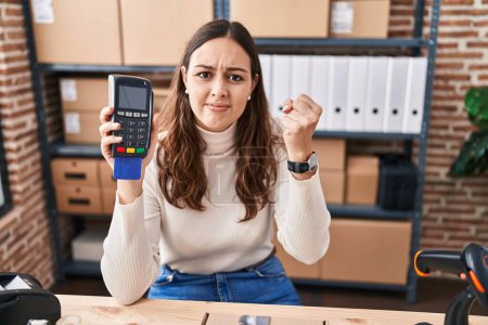 Photo for Young hispanic woman working at small business ecommerce holding dataphone annoyed and frustrated shouting with anger, yelling crazy with anger and hand raised - Royalty Free Image