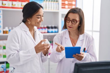 Photo for Two women pharmacist using touchpad holding pills at pharmacy - Royalty Free Image