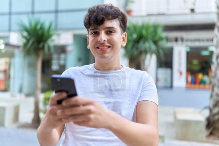 Téléchargez les photos : Homme non binaire souriant confiant en utilisant smartphone à la rue - en image libre de droit