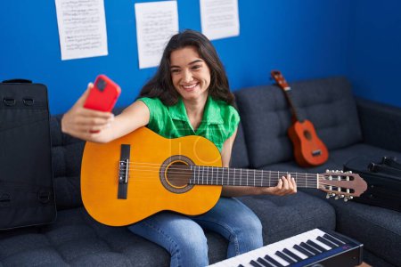 Téléchargez les photos : Jeune musicienne hispanique jouant de la guitare classique faire selfie par smartphone au studio de musique - en image libre de droit