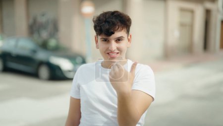 Téléchargez les photos : Non binaire homme souriant confiant faire geste à venir avec la main à la rue - en image libre de droit