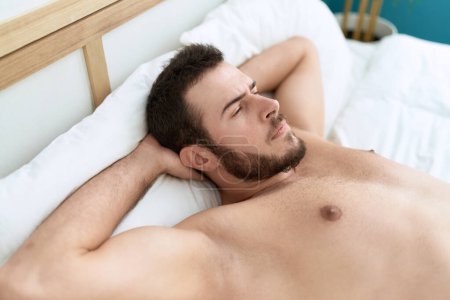 Foto de Young hispanic man lying on bed with relaxed expression at bedroom - Imagen libre de derechos