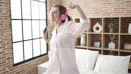 Téléchargez les photos : Young blonde woman listening to music and dancing on bed at bedroom - en image libre de droit