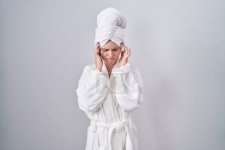 Foto de Mujer rubia caucásica usando albornoz con la mano en la cabeza, dolor de cabeza porque el estrés. padecer migraña. - Imagen libre de derechos