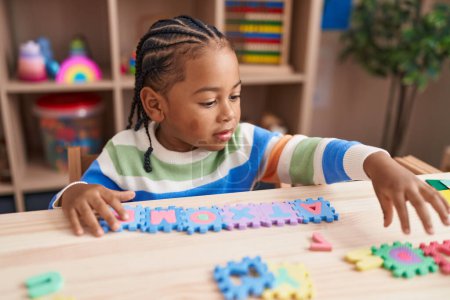 Foto de Niño afroamericano jugando con vocabulario juego de puzzle sentado en la mesa en el jardín de infantes - Imagen libre de derechos