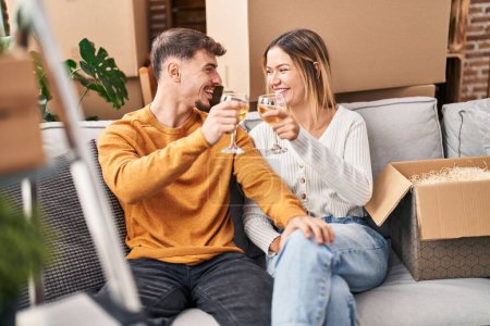 Foto de Joven pareja de hombres y mujeres brindando con vino sentado en un sofá en un nuevo hogar - Imagen libre de derechos