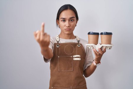 Téléchargez les photos : Young hispanic woman wearing professional waitress apron holding coffee showing middle finger, impolite and rude fuck off expression - en image libre de droit
