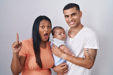 Photo for Young hispanic couple with baby standing together over isolated background pointing finger up with successful idea. exited and happy. number one. - Royalty Free Image